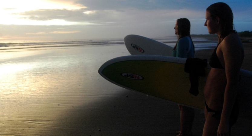 two people stand on the shore, holding surf boards and look out over the ocean